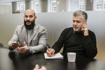 Homens sentados à mesa e discutindo projeto durante reunião de negócios — Fotografia de Stock