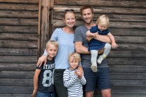 Famiglia posa all'aperto vicino a casa di legno e sorridente alla macchina fotografica — Foto stock