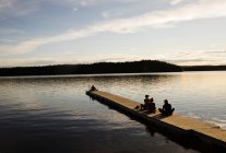 Mujeres jóvenes sentadas en un muelle de madera de un lago en Dalarna, Suecia. - foto de stock