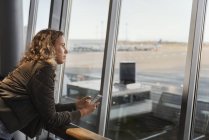 Mujer con teléfono inteligente por ventana del aeropuerto - foto de stock