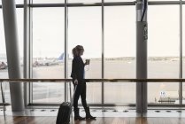 Frau mit Koffer und Smartphone am Flughafen — Stockfoto