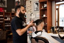 Barbier coupe les cheveux du client dans le salon de coiffure — Photo de stock