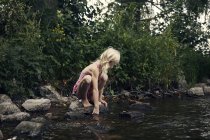 Vue latérale de fille accroupi par la rivière — Photo de stock