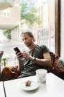 Молодий чоловік зі смартфоном у кафе, вибірковий фокус — стокове фото