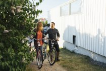 Pareja empujando bicicletas por casa - foto de stock