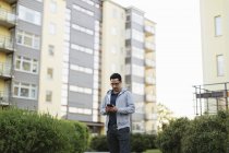 Чоловік використовує смартфон за багатоквартирним будинком — стокове фото