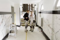 Pintores usando telefone inteligente no corredor do apartamento — Fotografia de Stock