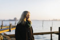 Junge Frau mit Mantel und Schal am Meer bei Sonnenuntergang — Stockfoto