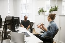 Молоді співробітники чоловічої статі сидять за столом і розмовляють в офісі — стокове фото