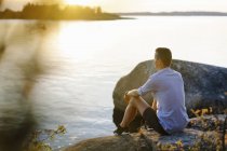 Uomo seduto sulla roccia per mare, attenzione selettiva — Foto stock