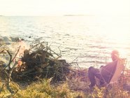 Hombre sentado junto a la hoguera por el mar, enfoque selectivo - foto de stock