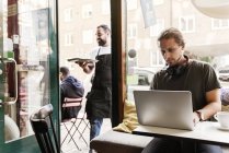 Молодой человек работает на ноутбуке в кафе — стоковое фото