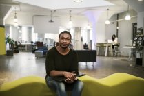 Mid adult man holding laptop and looking at camera while sitting on sofa in office — Stock Photo