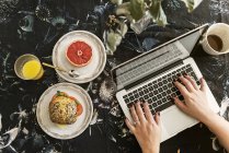 Hands of woman using laptop during breakfast — Stock Photo