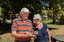 Portrait of happy senior couple using smartphone outdoors at sunny day — Stock Photo