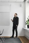 Man in earphones using smartphone in board room and looking aside — Stock Photo