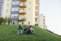 Pai e crianças sentados no gramado por prédio de apartamentos — Fotografia de Stock