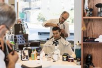 Отклонение парикмахера, стригущего волосы молодого человека в зеркале — стоковое фото