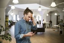 Орієнтований молодий чоловік використовує навушники зі смартфоном в офісі — стокове фото