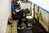 Chica en uniforme de hockey sobre hielo atando cordones en patines de hielo - foto de stock