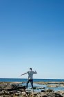 Hombre caminando descalzo sobre rocas por el mar, vista hacia atrás. - foto de stock
