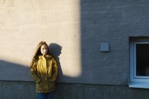 Menina vestindo capa amarela contra parede — Fotografia de Stock