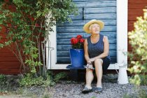 Senior woman sitting by flower pot in front of door — Stock Photo