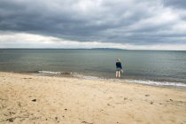 Вид ззаду жінки на піщаному пляжі, дивлячись на море — стокове фото