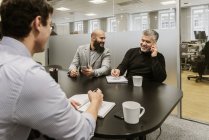 Hombres que discuten proyectos durante la reunión de negocios en el cargo - foto de stock
