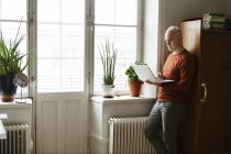 Hombre mayor usando el ordenador portátil por ventana - foto de stock