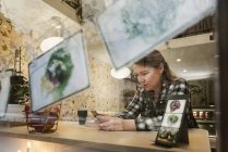 Donna con smartphone in caffetteria, vista attraverso il vetro — Foto stock