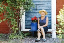 Femme âgée assise par pot de fleurs devant la porte — Photo de stock