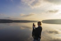 Femme adulte moyenne tenant un téléphone cellulaire devant le lac Aspen à Lerum, Suède — Photo de stock