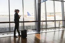 Mulher com mala e telefone inteligente no aeroporto — Fotografia de Stock