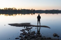 Чоловік стоїть на скелі в озері на заході сонця — стокове фото