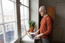 Uomo anziano utilizzando il computer portatile dalla finestra — Foto stock