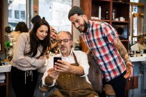 Усміхнені чоловічі та жіночі перукарі дивляться на смартфон — стокове фото