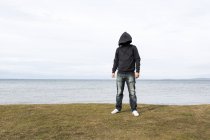 Uomo in felpa con cappuccio in piedi vicino al lago — Foto stock