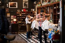 Barbieri che tagliano capelli di clienti in negozio di barbiere — Foto stock