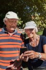 Porträt eines glücklichen Senioren-Paares, das an sonnigen Tagen sein Smartphone im Freien benutzt — Stockfoto
