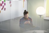 Молодий зосереджений чоловік сидить в офісі і використовує смартфон за допомогою лампи — стокове фото