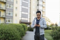 Hombre usando el teléfono inteligente por edificio de apartamentos - foto de stock