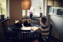 Мальчик читает книгу, сидя за обеденным столом — стоковое фото