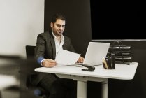 Молодой человек, сидящий за партой и работающий с ноутбуком в офисе — стоковое фото
