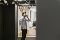 Giovane uomo in piedi con mano in tasca e parlare al telefono in ufficio — Foto stock