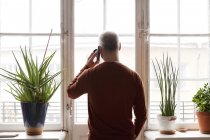 Hombre mayor usando el teléfono inteligente por ventana - foto de stock