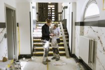 Pintores usando teléfono inteligente en el pasillo del apartamento - foto de stock