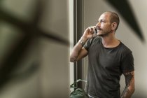Mittlerer erwachsener Mann mit Smartphone und Blick auf Fenster, selektiver Fokus — Stockfoto