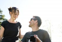 Пара улыбается друг другу и пользуется смартфоном на улице — стоковое фото
