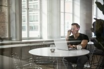 Young man using laptop and talking on phone, selective focus — Stock Photo